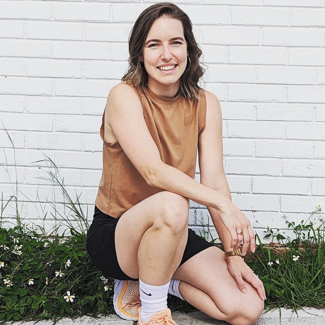 Avery Howard kneeling and smiling in front of a white brick wall