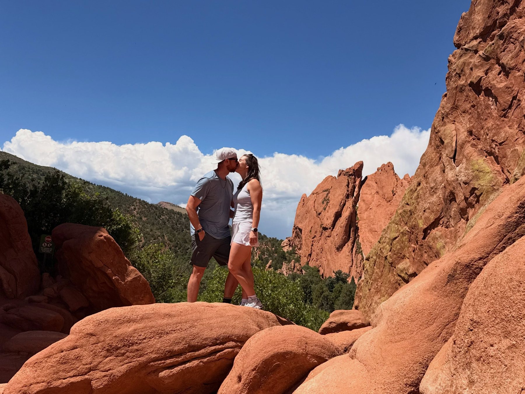 Kyle and Avery kissing on red rock formations under a blue Colorado sky