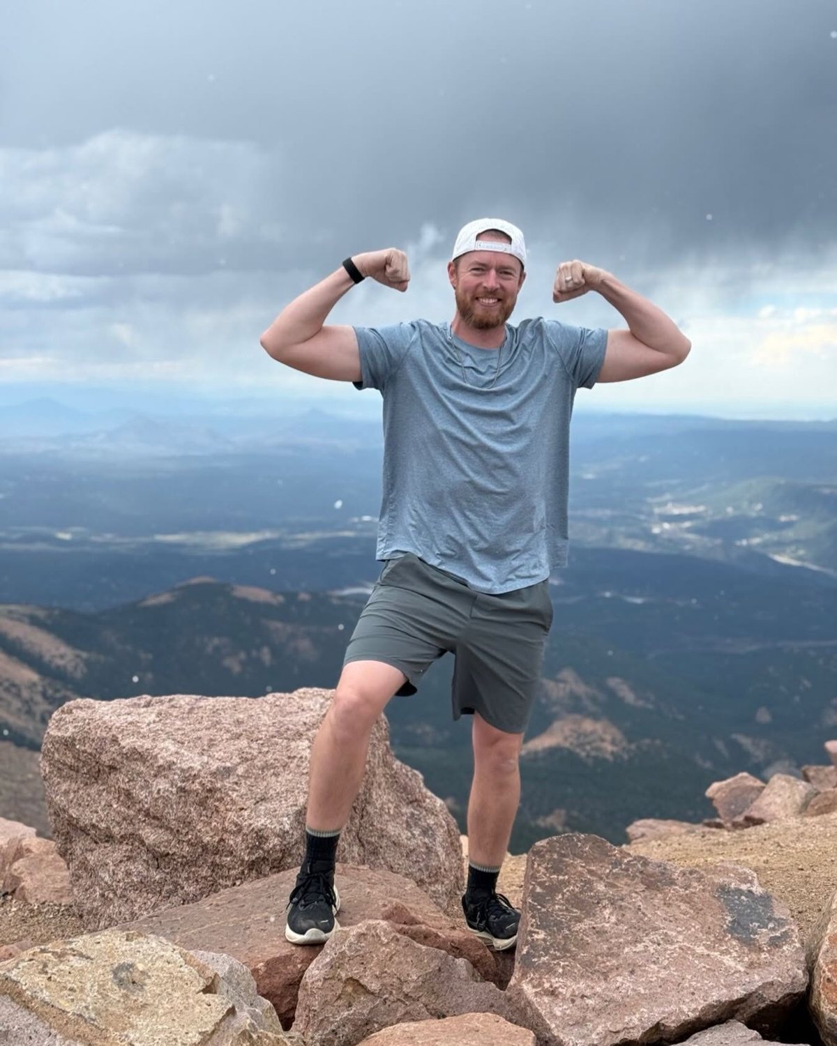 Kyle Howard flexing at a rocky mountain summit under storm clouds